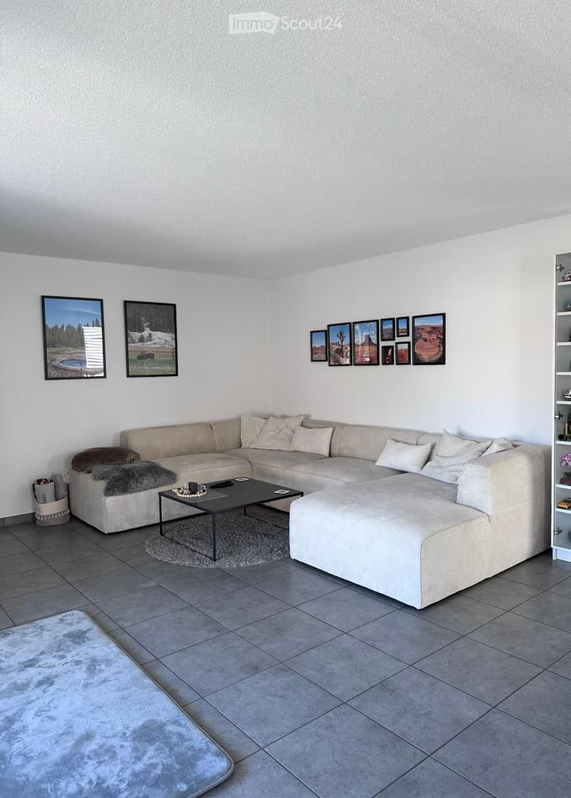 Modern living room with a large L-shaped sofa, coffee table, ottoman, and picture frames on the wall.