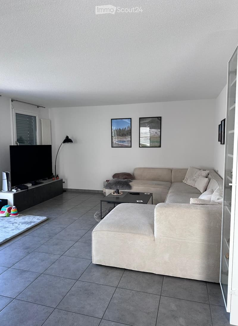 Modern living room with grey sectional sofa, coffee table, floor lamp, TV stand, and picture frames on the wall.