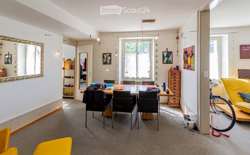 Bright living space with a yellow sofa, dining table with chairs, bicycle, and various decorative items including mirrors and artwork.