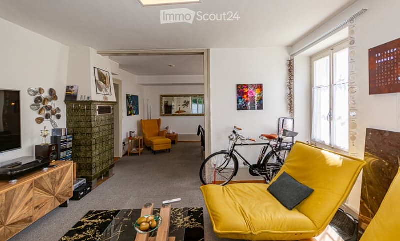 Bright living room with a yellow sofa, coffee table, armchair, television, bicycle, and artwork on the walls.