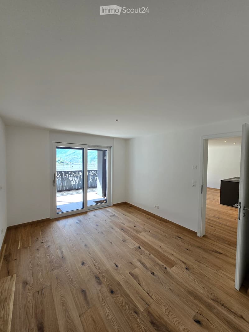 Empty room with wooden flooring, white walls, and a sliding glass door leading to a balcony.