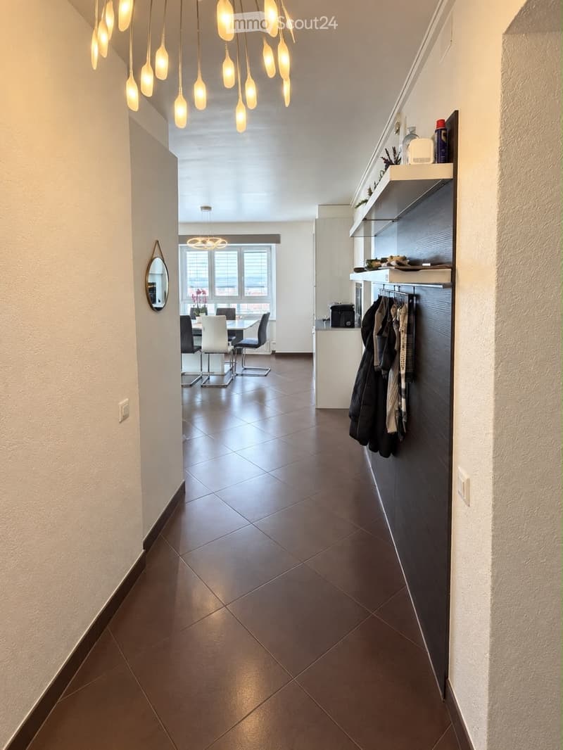 Modern hallway with dark tiled floor, white walls, pendant lights, and a small dining area visible at the end.