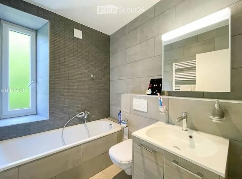 Modern bathroom with a bathtub, toilet, sink, mirror, and cabinet. Features a large window with a view, sleek fixtures, and a clean, contemporary design.