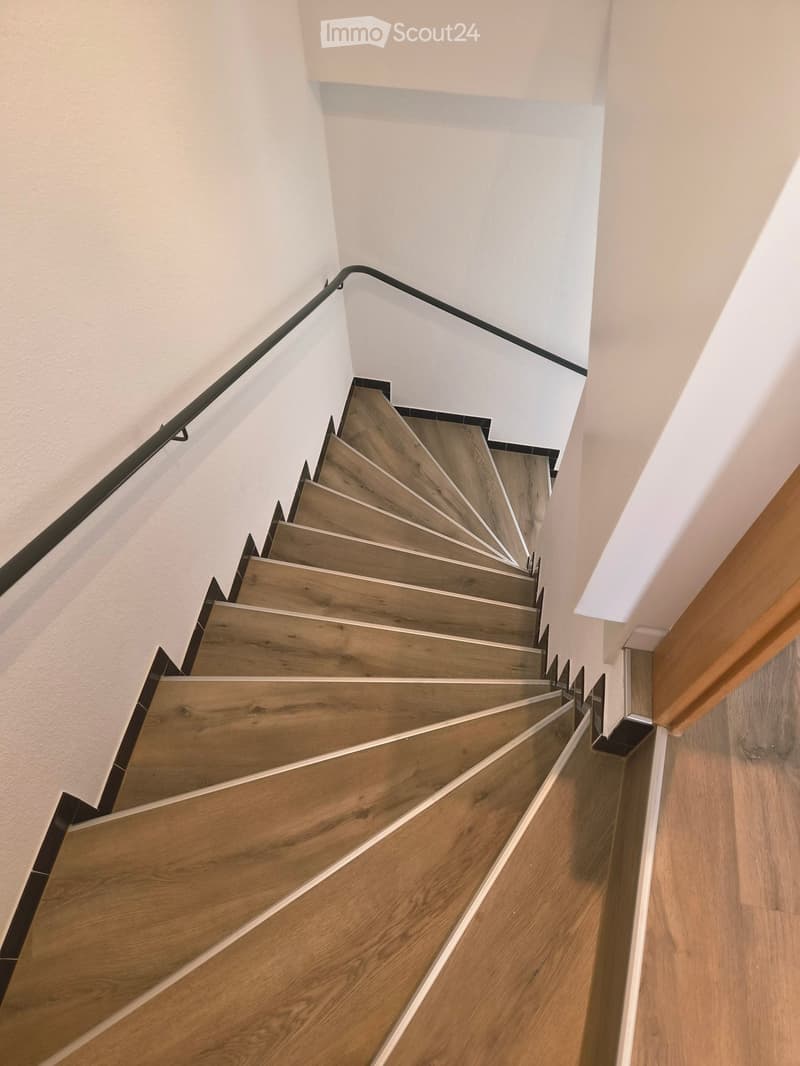 Wooden staircase with modern design, featuring a sleek black metal railing and wooden steps.