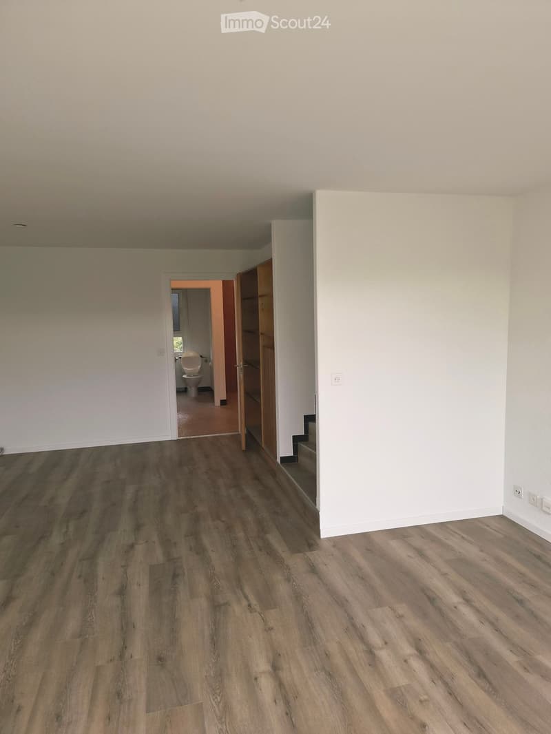 Empty room with wooden flooring and white walls, featuring an open doorway leading to a bathroom with a toilet visible.