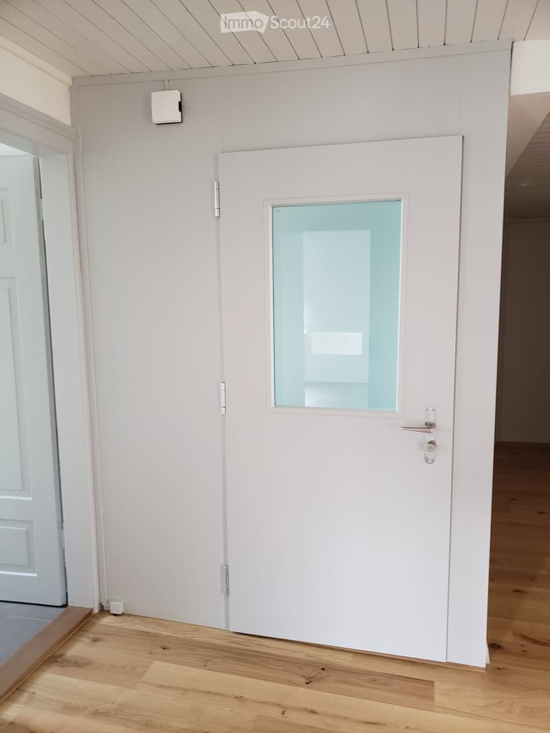 Empty hallway with white walls, wooden flooring, and a white door with a frosted glass panel.