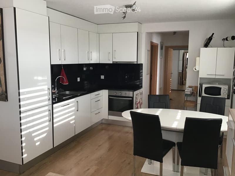 Modern kitchen with white cabinets, stainless steel appliances, and a round dining table with four black chairs.