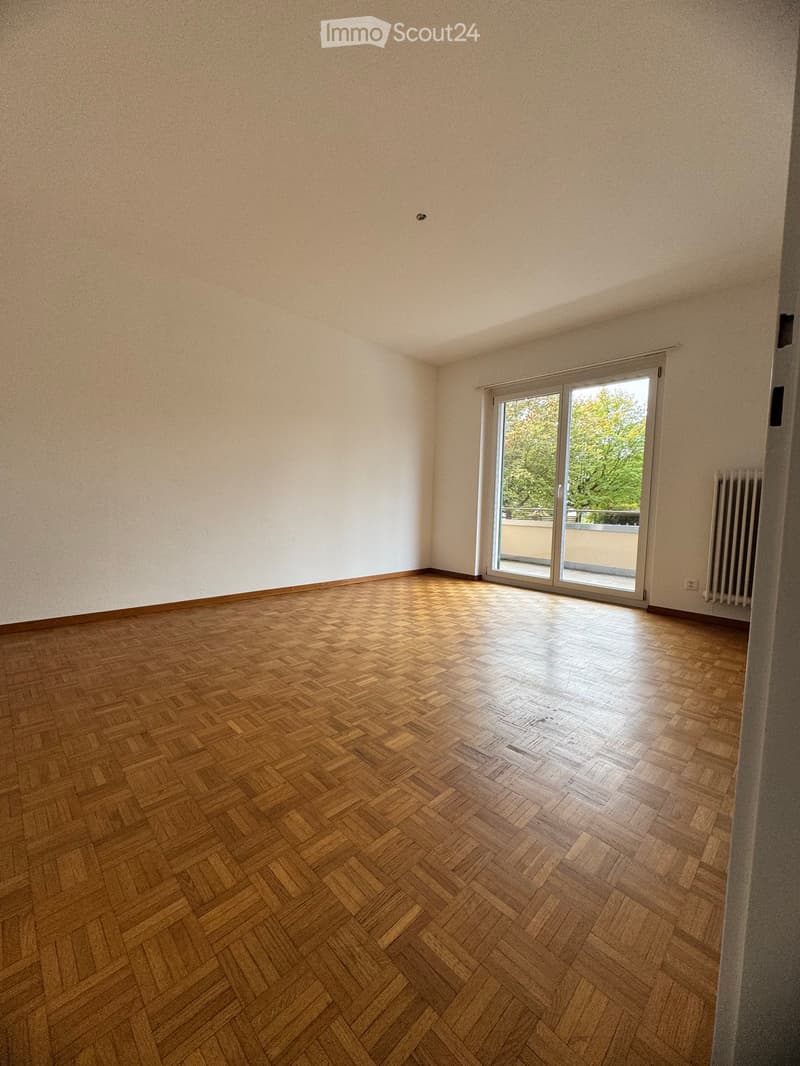 Empty room with wooden herringbone flooring, white walls, and a sliding glass door leading to a balcony.