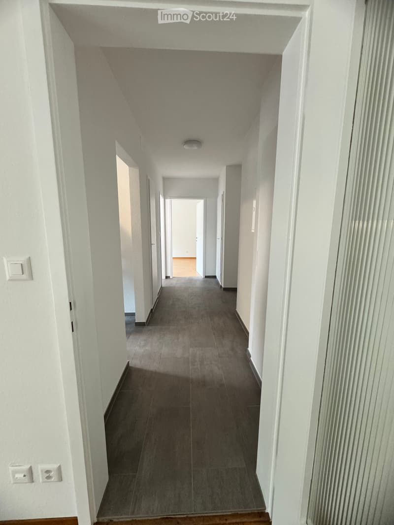 Empty hallway with tiled floor, white walls, and multiple doors leading to other rooms.