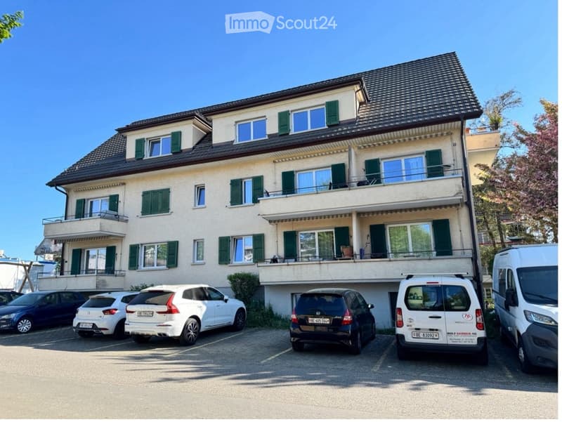 3 story apartment building, beige exterior, green shutters, multiple balconies, parking lot