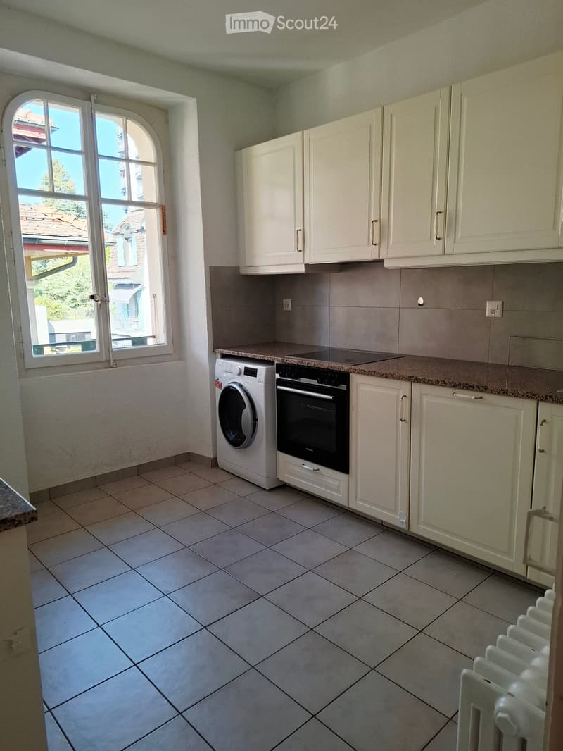 Bright kitchen with white cabinets, tiled floor, and a window offering a view of the outside. Includes a washing machine and an oven.