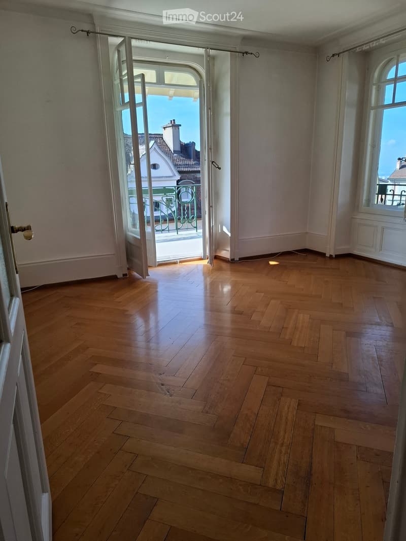 Empty room with wooden flooring, large open doorway leading to a balcony, and large windows allowing natural light.