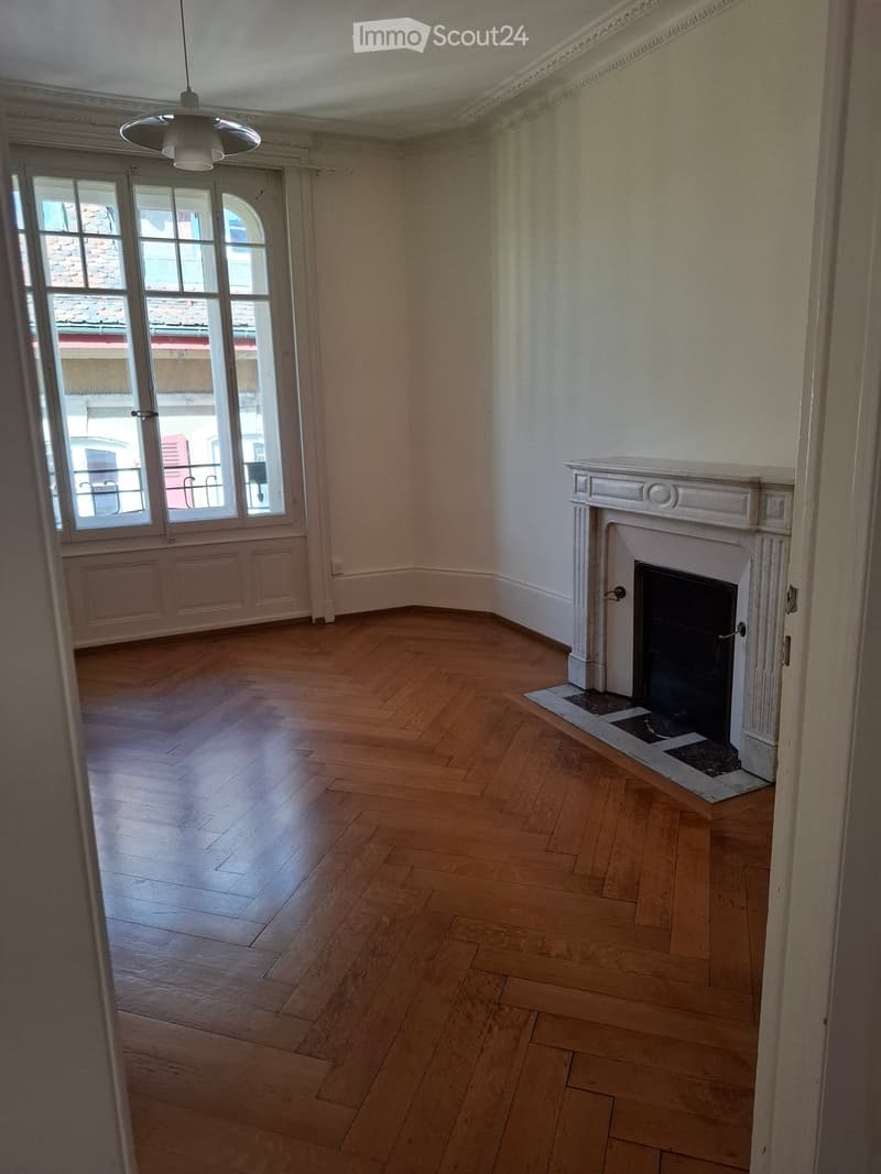 Empty room with wooden flooring, large windows, and a fireplace with a decorative mantel.