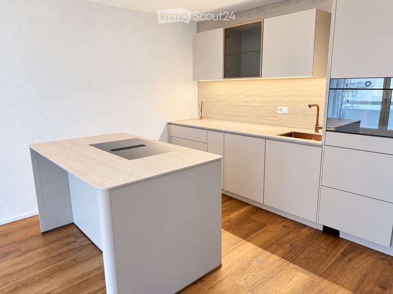 Modern kitchen with light-colored cabinets, a central island with a built-in sink, and a sleek faucet. The space features wooden flooring and built-in lighting above the counter.