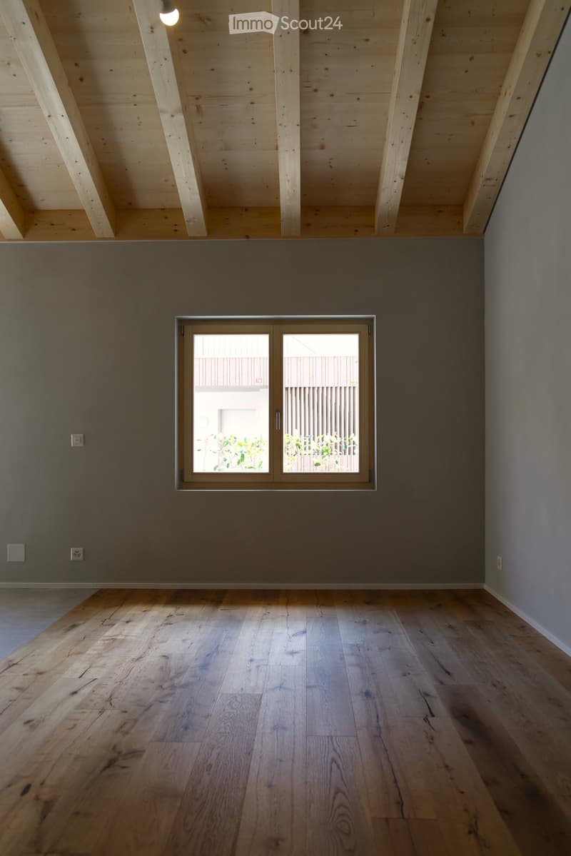 Empty room with wooden floor, grey walls, and a large window with double doors leading outside.