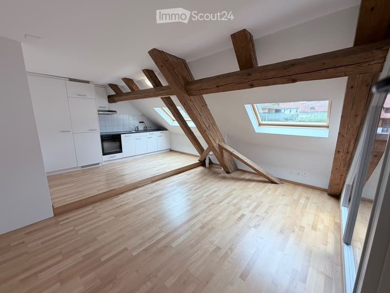 Empty attic space with wooden beams, wooden flooring, white cabinets, and skylight windows.