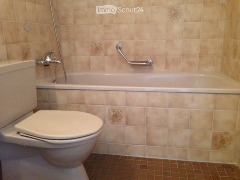 Bathroom with beige tiled walls and floor, a toilet, a bathtub, and a silver grab bar.