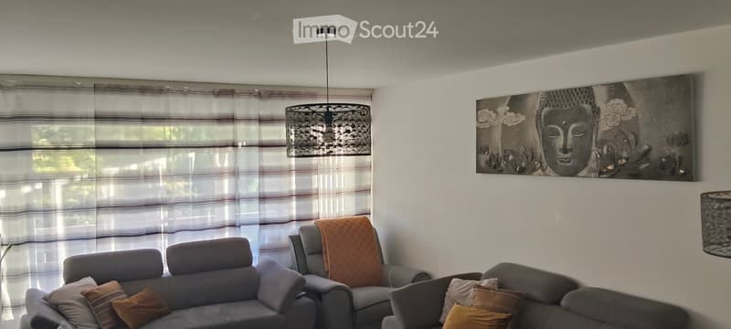 Living room with grey sofa, armchair, throw pillows, wall art, and a large window with striped curtains.