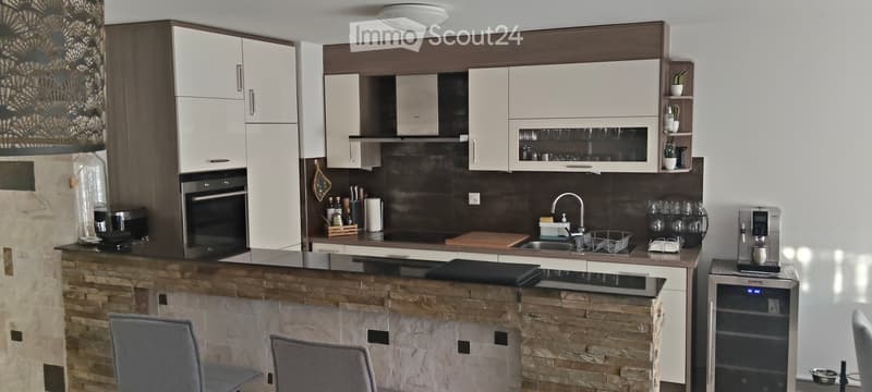 Modern kitchen with white cabinets, dark countertops, and a stone island. Includes a sink, faucet, oven, coffee maker, and stools.