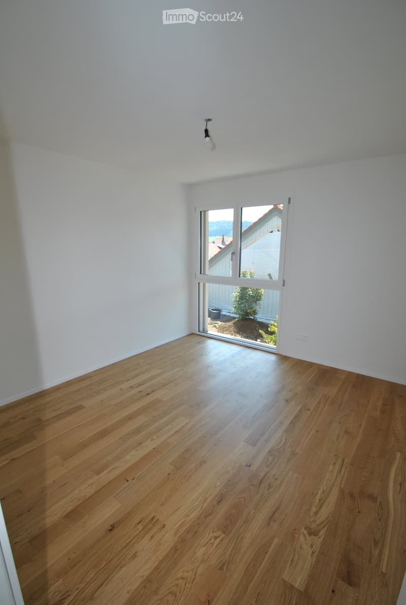 Empty room with light wooden flooring and white walls, featuring a large sliding glass door leading to an outdoor area.