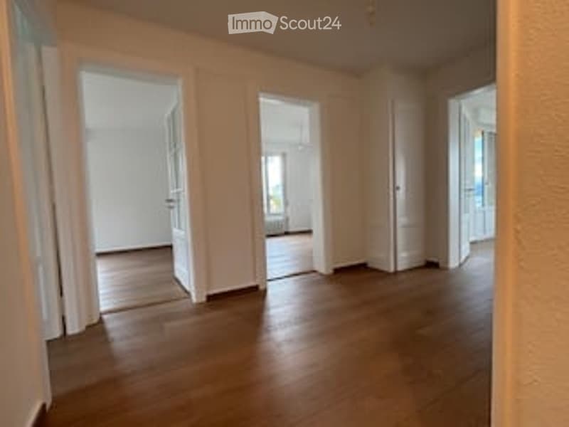 Empty room with wooden flooring and white walls, multiple open doorways leading to other spaces.