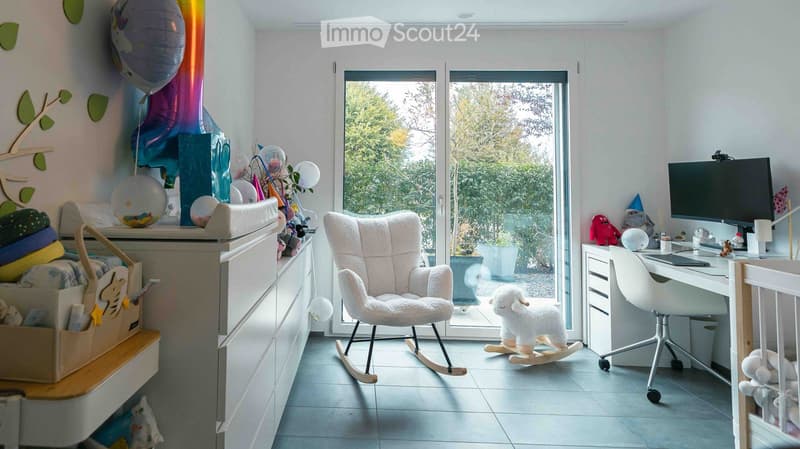 A well-lit room with a rocking chair, desk, and various toys and decorations, including balloons and a small white rocking stool.