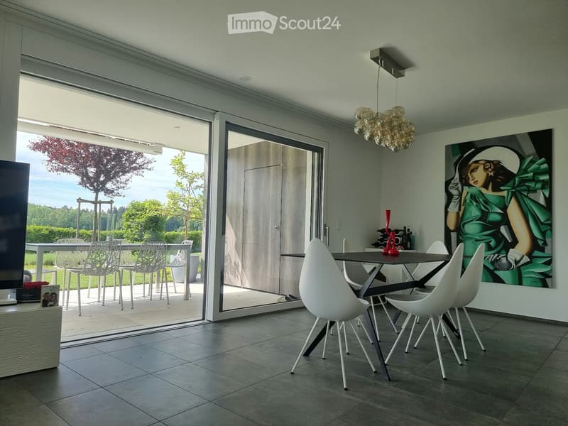 Modern dining room with large sliding glass doors leading to a patio, white chairs, a black dining table, a wine rack, and a large artwork on the wall.