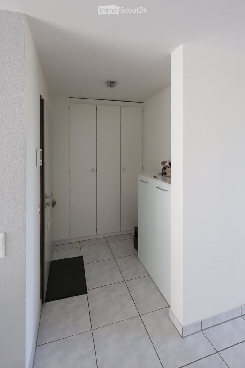 A clean, narrow hallway with tiled flooring, white walls, and built-in storage cabinets. A small black mat is placed near the entrance.