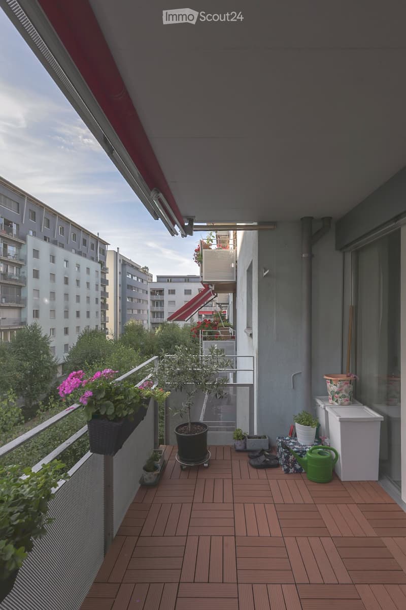 Balcony with wooden decking, potted plants, garden hose, and small storage stool.
