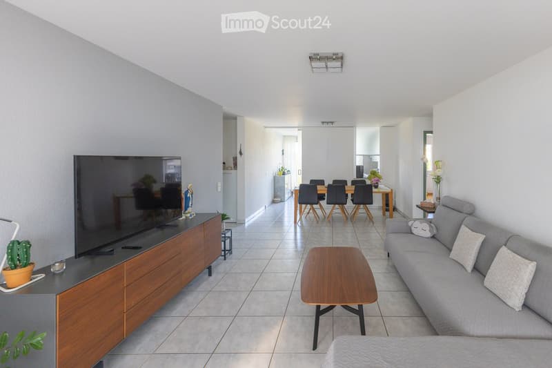 Modern living room with grey sofa, wooden coffee table, TV stand, and dining area with chairs and table.