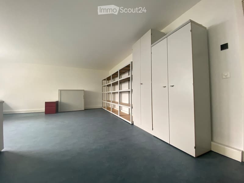 Empty room with grey carpeted floor, white walls, and built-in storage units including a tall cabinet and a shelving unit. A small red chest is visible near the wall.