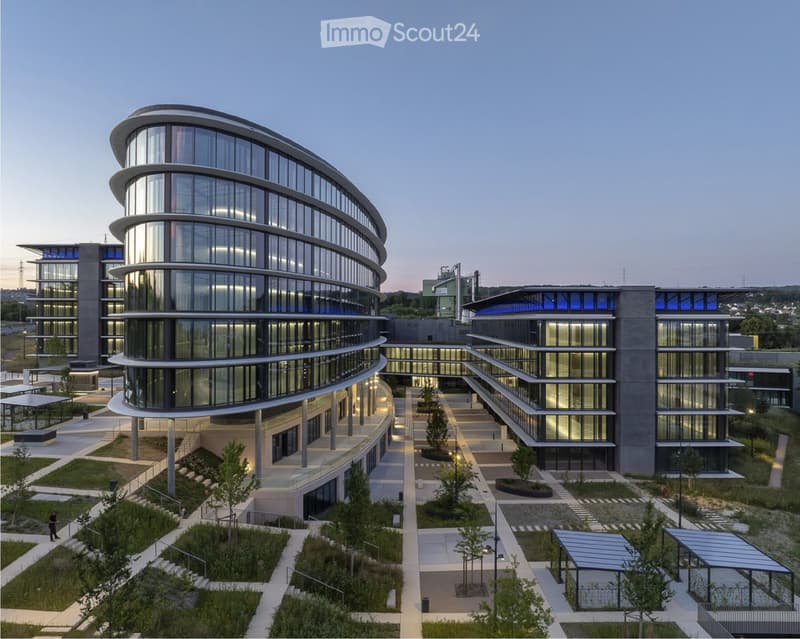 Modern multi-story building with a curved glass facade, surrounded by landscaped gardens and pathways.