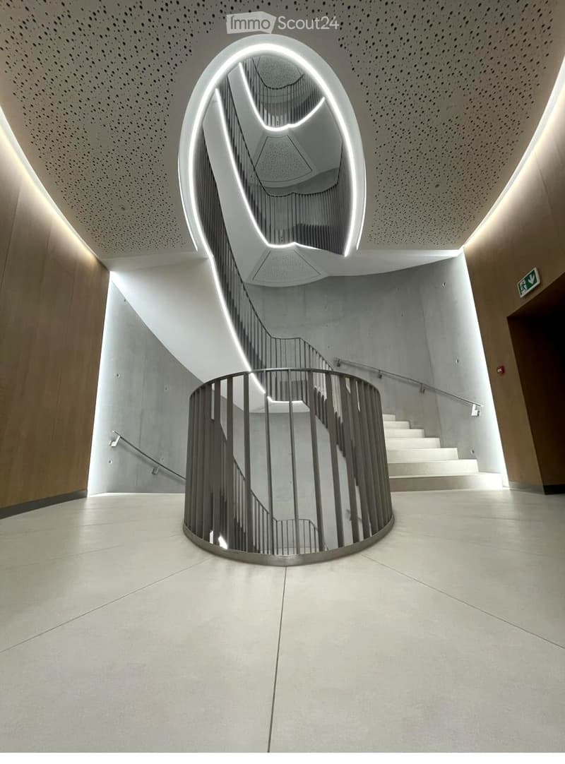Modern interior hallway with a central, illuminated, sculptural staircase featuring a curved, metallic railing and white steps.