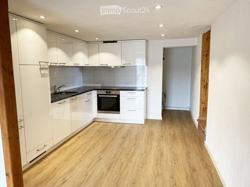 Modern kitchen with white cabinets, a black countertop, and a wooden floor. Features include a sink, oven, and faucet.