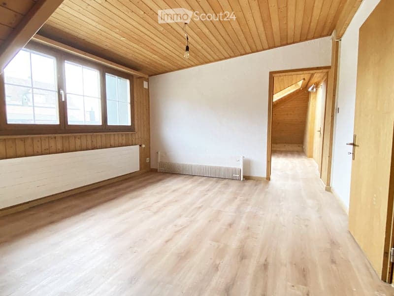 Empty room with wooden flooring, white walls, large windows, and exposed wooden beams on the ceiling. No furniture or equipment present.