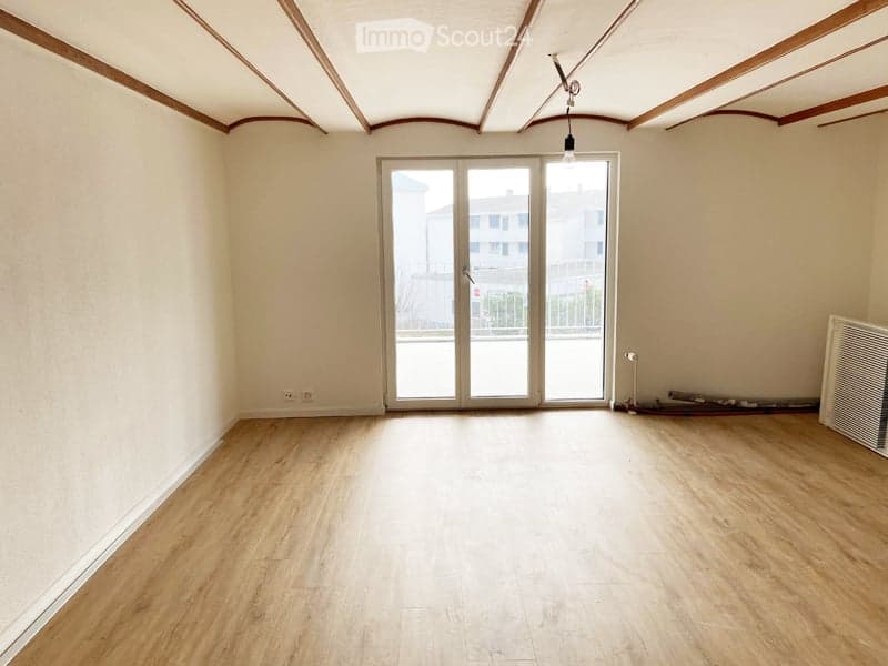 Empty room with wooden flooring, white walls, large glass sliding doors leading to a balcony, and a simple ceiling light fixture.