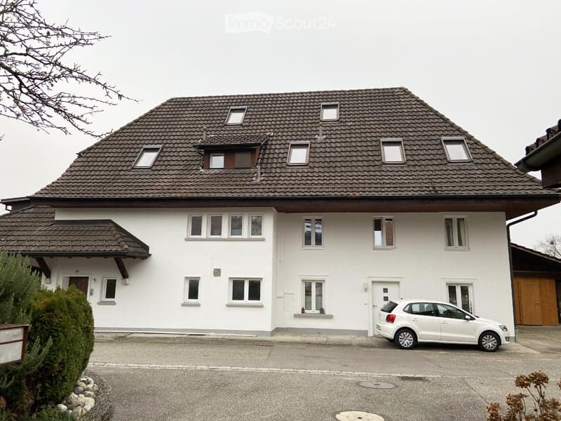Two-story white house with a brown tiled roof, multiple windows, and a parked car in the driveway.