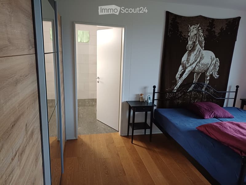Bedroom with wooden flooring, a single bed with blue mattress and pink pillows, a nightstand with small items, a large wall tapestry of a horse, and a mirror on the left side.