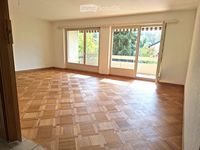 Empty room with wooden parquet flooring, large windows, and sliding glass doors leading to a balcony.