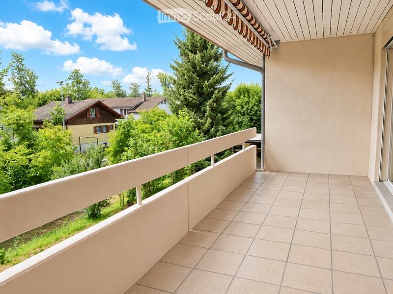 Balcony with tiled floor, beige railing, and a view of greenery and neighboring houses.
