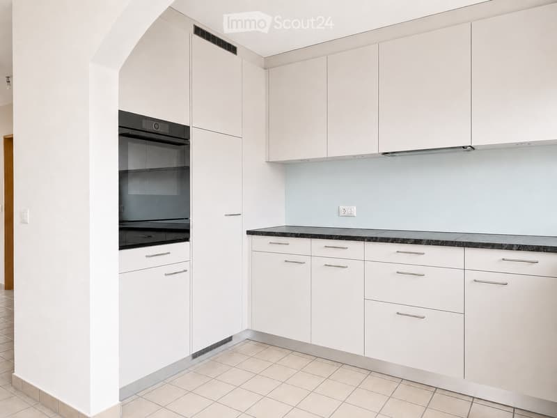 Modern kitchen with white cabinets, black countertop, and built-in oven. Light blue backsplash and tiled floor.