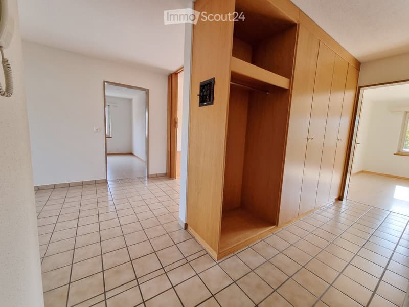 Empty hallway with tiled floor, wooden closet, and open doors leading to other rooms.