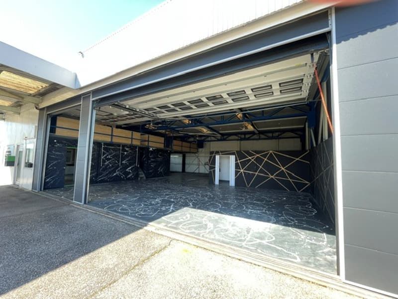 Large, open garage space with a high ceiling, industrial-style lighting, and a polished concrete floor. The space is empty, with no furniture or equipment visible.