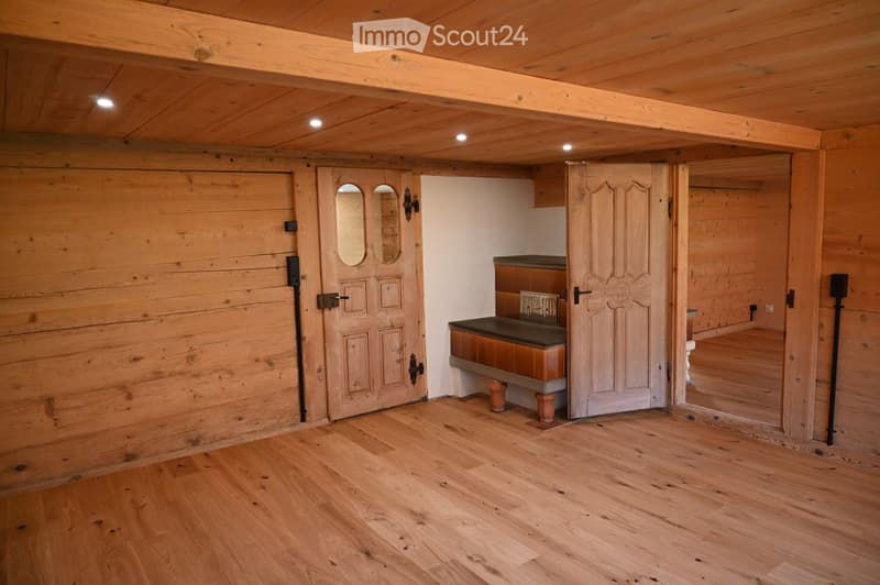 Empty room with wooden walls and ceiling, polished wooden floor, and a small bench with a cushioned seat in the corner.