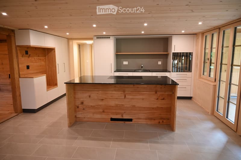 Modern kitchen with a wooden island, white cabinets, and a black countertop. The space features large windows and recessed lighting.