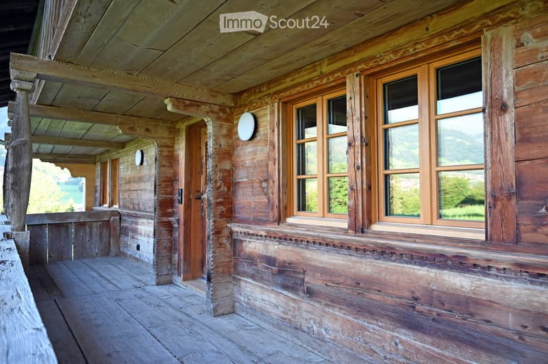 Wooden balcony with large windows, wooden floor, and scenic mountain view.
