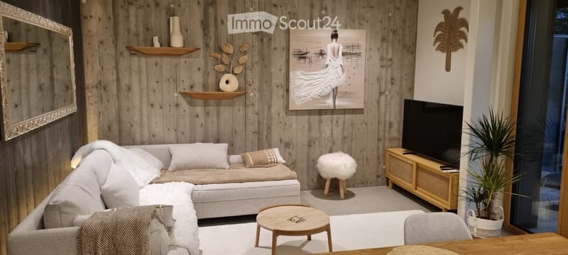 Modern living room with wooden walls, a grey sectional sofa, a small coffee table, a TV stand, a decorative stool, and a large painting on the wall.