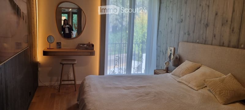Cozy bedroom with a wooden bed, nightstand, mirror, and a small desk with a stool.