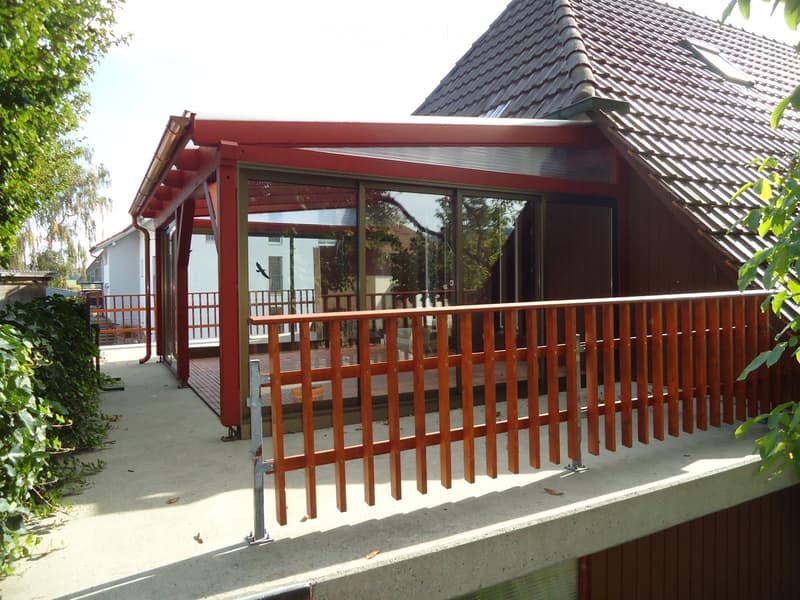 Balcony with wooden railing, glass-enclosed section, and a view of the surrounding area.