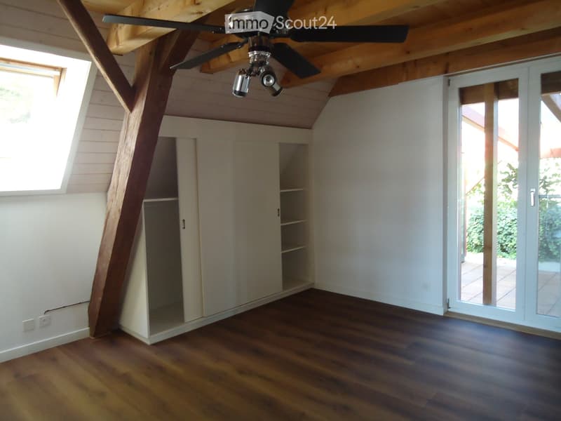 Empty room with wooden flooring, white walls, large window, sliding glass door, built-in closet, and exposed wooden ceiling beams.